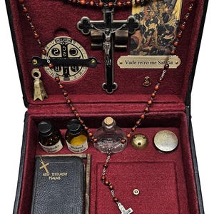 Puede incluir: Una caja negra con interior de terciopelo rojo, que contiene objetos religiosos. Incluye un crucifijo, cuentas de rosario, un libro peque&ntilde;o, viales y una imagen peque&ntilde;a. La caja se cierra con un pestillo y tiene detalles dorados.