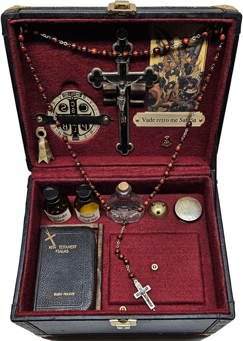 Puede incluir: Una caja negra con interior de terciopelo rojo, que contiene objetos religiosos. Incluye un crucifijo, cuentas de rosario, un libro peque&ntilde;o, viales y una imagen peque&ntilde;a. La caja se cierra con un pestillo y tiene detalles dorados.