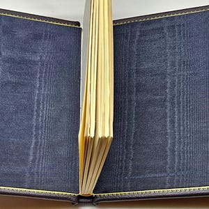 May include: A dark blue leather-bound journal with gold stitching and decorative clasps. The journal is open to reveal blank pages.