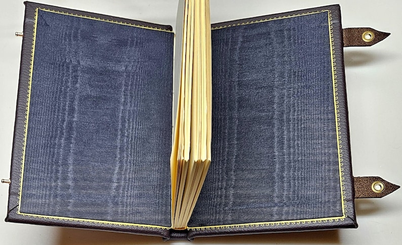 May include: A dark blue leather-bound journal with gold stitching and decorative clasps. The journal is open to reveal blank pages.