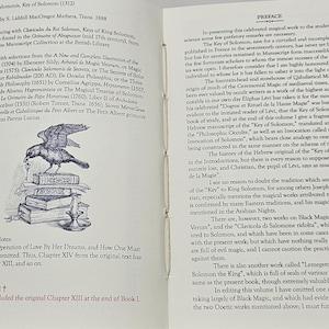 May include: A vintage book, open to reveal text and an illustration of a bird atop a pile of books. The title "Clavicula Salomonis, Key of Solomon" is displayed. The pages are aged, with a preface on the right-hand page.