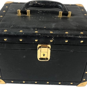 Puede incluir: Caja negra vintage con herrajes dorados. La caja tiene un asa en la parte superior y un cierre de pestillo en la parte delantera. Los protectores de esquina y los remaches dorados se suman a la est&eacute;tica vintage de la caja. La caja mide aproximadamente 25 cm de ancho, 20 cm de profundidad y 20 cm de alto.