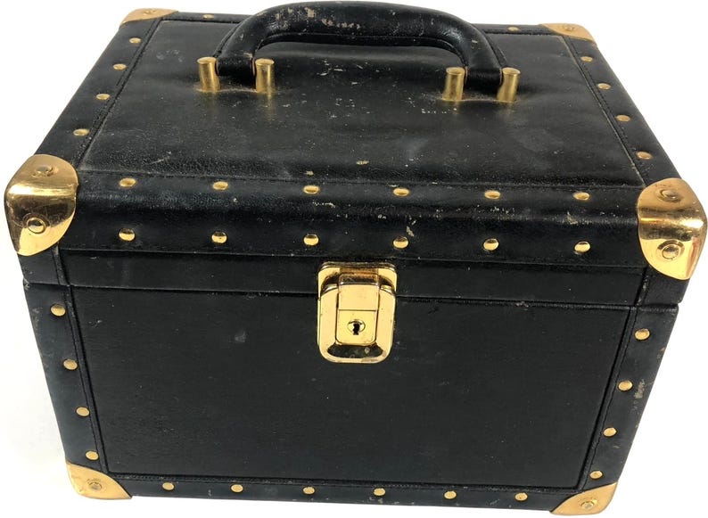 Puede incluir: Caja negra vintage con herrajes dorados. La caja tiene un asa en la parte superior y un cierre de pestillo en la parte delantera. Los protectores de esquina y los remaches dorados se suman a la est&eacute;tica vintage de la caja. La caja mide aproximadamente 25 cm de ancho, 20 cm de profundidad y 20 cm de alto.