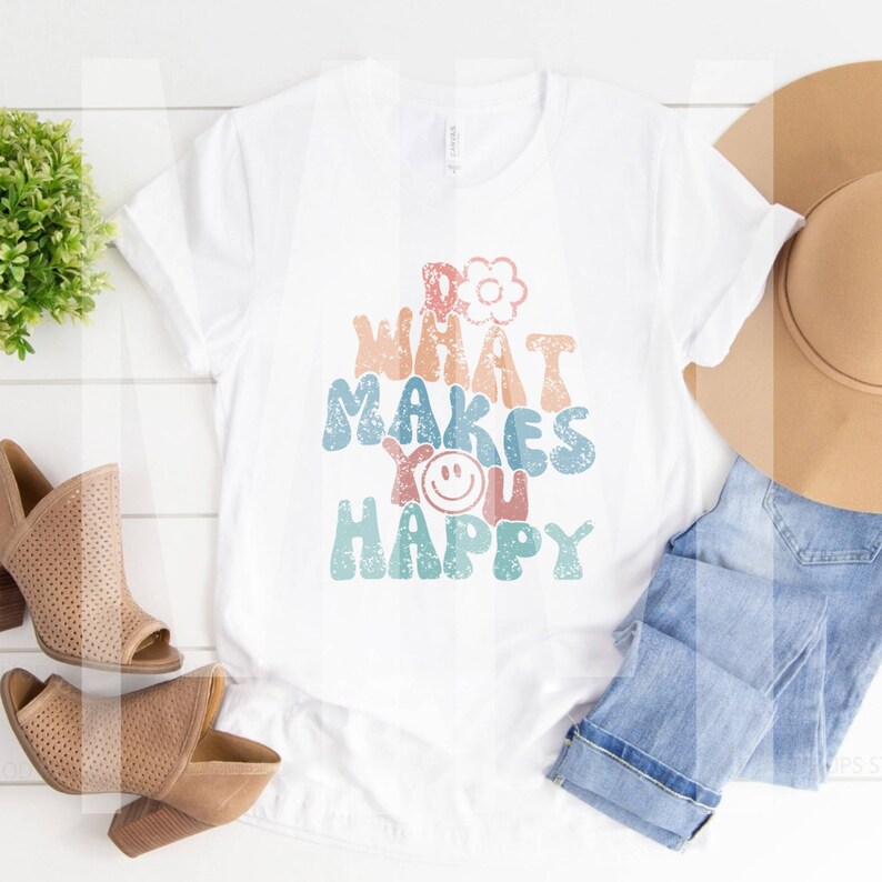May include: White t-shirt with a retro-style graphic that says "Do What Makes You Happy". The graphic is in shades of blue, pink, and green with a flower and a smiley face.
