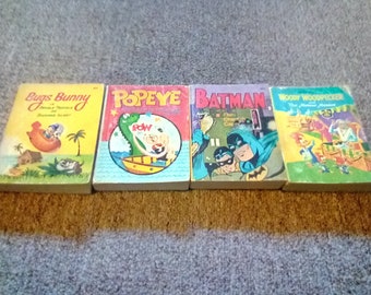 May include: Four vintage paperback books featuring popular cartoon characters: Bugs Bunny, Popeye, Batman, and Woody Woodpecker. The books have colourful covers with illustrations of the characters.