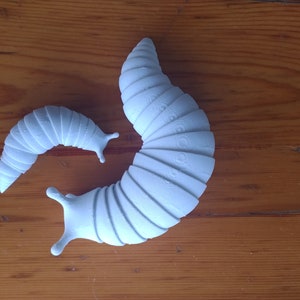May include: Two light blue segmented, plastic, toy millipedes. The larger millipede is curled into a C shape. The smaller millipede is straight and is positioned behind the larger millipede.