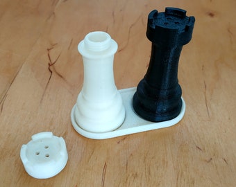 Może przedstawiać: Zestaw ceramicznych solniczek i pieprzniczek w kolorze białym i czarnym, w kształcie pionków szachowych. Solniczki stoją na białej podstawie i są gotowe, aby dodać odrobinę fantazji do Twojej kuchni.