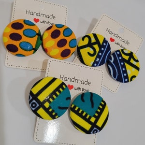 May include: Three pairs of handmade fabric earrings with colorful geometric patterns. The earrings are yellow, blue, green, and black. Each pair is displayed on a white card with the text "Handmade with love".