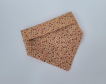 May include: A tan fabric bandana featuring a floral pattern of small red and purple flowers with green stems. The bandana is folded over, creating a layered effect. The fabric has a soft, slightly textured appearance.