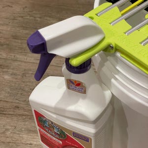 May include: White plastic spray bottle with a purple and green sprayer. The bottle has a label that reads "Captain Jack's Deadbug" and "For Organic Gardening". The sprayer is attached to a white bucket.