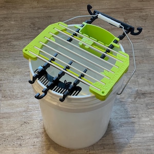 May include: A green and black plant potty system with a white bucket. The system includes a green frame with metal bars, a small green container, and black hooks. The words "PLANTA POTTY" are printed on the green frame.