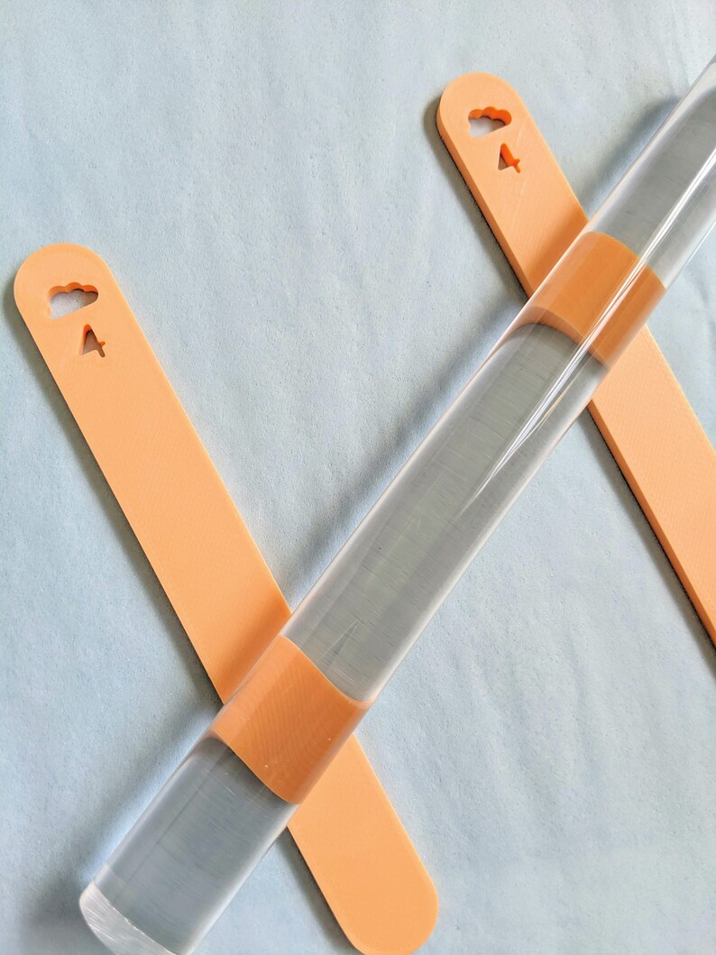 May include: Two orange rolling pins with cloud and airplane cutouts. The rolling pins are made of clear acrylic and have a textured surface.