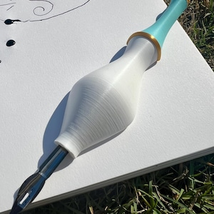 May include: A calligraphy pen featuring a white, bulbous, 3D-printed handle with a smooth texture. The upper section of the handle is light blue with a gold-colored ring accent. A silver metal nib is inserted into the base of the white handle.