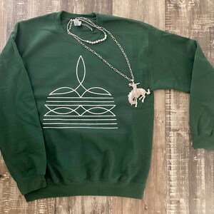 May include: A dark green sweatshirt with a white geometric design and a silver pendant necklace featuring a horse rider.