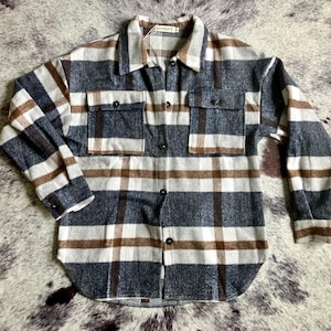 May include: A button-down flannel shirt in a plaid pattern of navy blue, white, and brown. The shirt has two chest pockets and a collar. The sleeves are long, and the shirt is made of a soft, woven fabric.