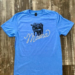 May include: A light blue t-shirt with a black silhouette of a cow and calf with the word "Mama" in rhinestones.
