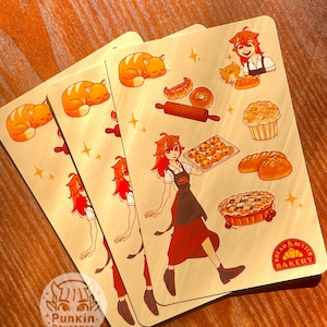 May include: Three rectangular stickers with a bakery theme. Each sticker features a red-haired person in a baker's apron, baked goods, and a sleeping orange cat. The stickers have the text "Bread & Butter Bakery" and "Punkin Pancakes".