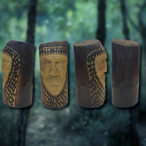 May include: Four wooden carvings of faces, each with a different expression, are carved into the side of a log. The carvings are detailed and realistic, with intricate patterns around the faces.