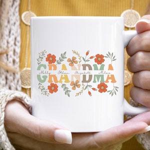 May include: White ceramic mug with the word "GRANDMA" in retro orange, green, and tan lettering, adorned with floral accents and the names Molly, Ethan, Elizabeth, and Miles. The mug has a white handle.
