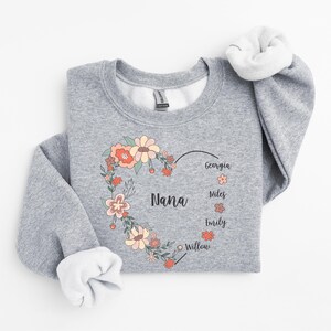 Pode incluir: Camisola cinzenta com um design de cora&ccedil;&atilde;o floral que diz "Nana" e os nomes Georgia, Miles, Emily e Willow.