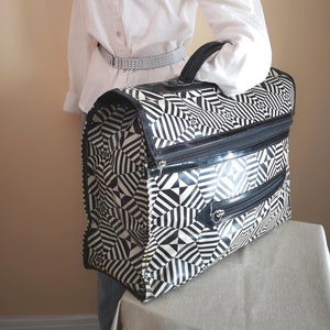 Peut inclure: Un sac de voyage à motif géométrique noir et blanc avec une fermeture éclair noire et une poignée argentée.