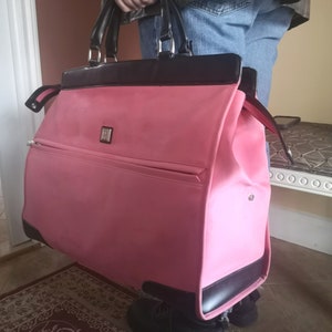Peut inclure: Sac de voyage rose et noir avec une poche zippée et une poignée noire.