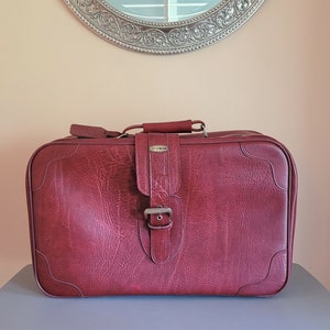 Peut inclure: Une valise vintage en cuir bordeaux avec une boucle argentée et le mot "Jet Stream" en relief sur le devant.