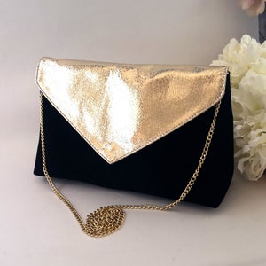 Op de afbeelding: Een zwarte en gouden clutch met een kettingband. De tas heeft een klep sluiting en een gouden metallic afwerking aan de voorkant.