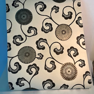May include: Black and white wallpaper with a repeating pattern of stylized flowers and swirling vines. The flowers have a gray center and a black outline.