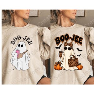 May include: A beige sweatshirt featuring two ghost designs with the text BOO-JEE. The left ghost wears a crossbody bag and holds a pink tumbler. The right ghost wears a leopard print bow and sunglasses, holding a leopard print bag and a drink.