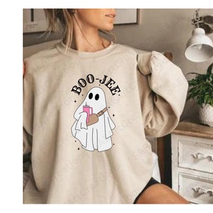 May include: A beige sweatshirt featuring a graphic of a ghost holding a pink drink and the text "BOO-JEE".