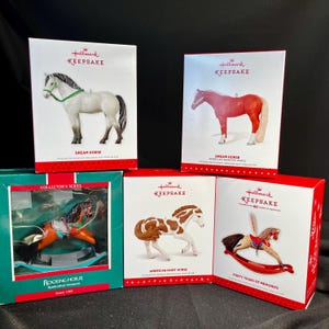 May include: A collection of Hallmark Keepsake horse ornaments in their original boxes. The ornaments include a white Dream Horse, a red American Quarter Horse, a Rocking Horse, and an American Paint Horse. The boxes are red, white, and green.