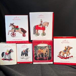 May include: A collection of Hallmark Keepsake ornaments featuring a rocking horse, a pony on wheels, and a pony pulling a sleigh. The ornaments are all red and white with gold accents. The text on the boxes reads "Hallmark Keepsake" and "A Pony for Christmas".