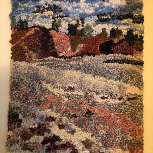 May include: A textured wall hanging depicting a landscape scene. The top portion features a blue sky with white clouds. Below, a brown and pink landscape with green trees transitions into a gray and pink foreground.