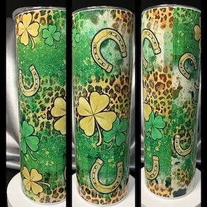 Puede incluir: Un vaso de acero inoxidable verde y dorado con estampado de leopardo, tréboles de cuatro hojas y herraduras doradas.