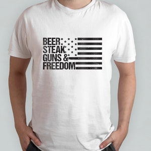 May include: White t-shirt with a black and white American flag design. The text "BEER, STEAK, GUNS & FREEDOM" is printed on the shirt.