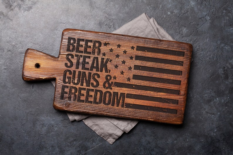 May include: Wooden cutting board with an American flag design and the text "Beer, Steak, Guns & Freedom".