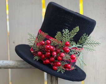 May include: A black top hat with a red and black plaid ribbon and red berries and green sprigs.