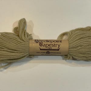 May include: A skein of beige Needlepoint Tapestry Yarn, made of 100% pure virgin wool. The yarn is wrapped around a tan cardboard tube with the brand name and product details printed on it. The yarn is a light, neutral color.