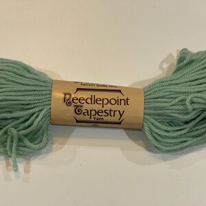 May include: A skein of mint green Needlepoint Tapestry Yarn. The yarn is wrapped around a brown paper label with the words "Needlepoint Tapestry Yarn" in a decorative font. The yarn is a soft, thick texture.