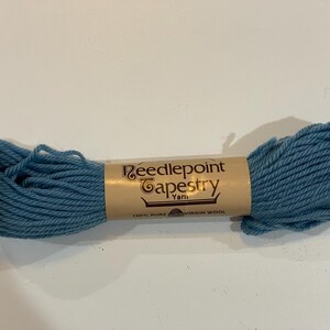 May include: A skein of blue Needlepoint Tapestry Yarn. The yarn is wrapped around a tan paper label with the words "Needlepoint Tapestry Yarn" printed on it. The label also states "100% Pure Virgin Wool".