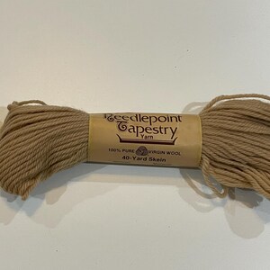 May include: A skein of Needlepoint Tapestry Yarn in a light brown color. The label reads "100% Pure Virgin Wool, 40-Yard Skein". The yarn is tightly wound and ready for crafting projects. Ideal for needlepoint and other textile arts.