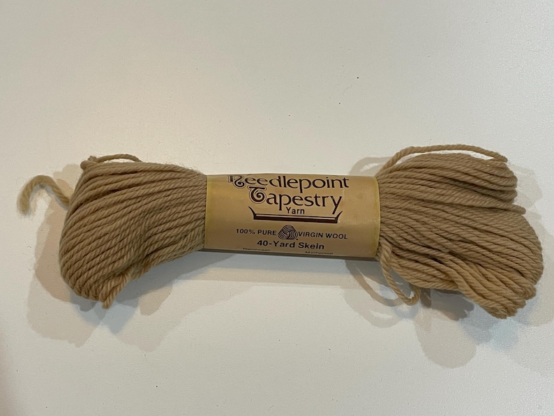 May include: A skein of Needlepoint Tapestry Yarn in a light brown color. The label reads "100% Pure Virgin Wool, 40-Yard Skein". The yarn is tightly wound and ready for crafting projects. Ideal for needlepoint and other textile arts.