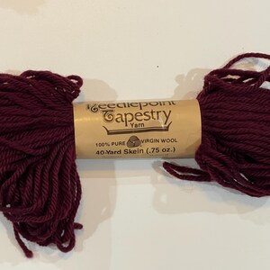 May include: A skein of burgundy wool yarn labeled "Needlepoint Tapestry Yarn" with the details "100% Pure Virgin Wool, 40-Yard Skein (.75 oz.)"