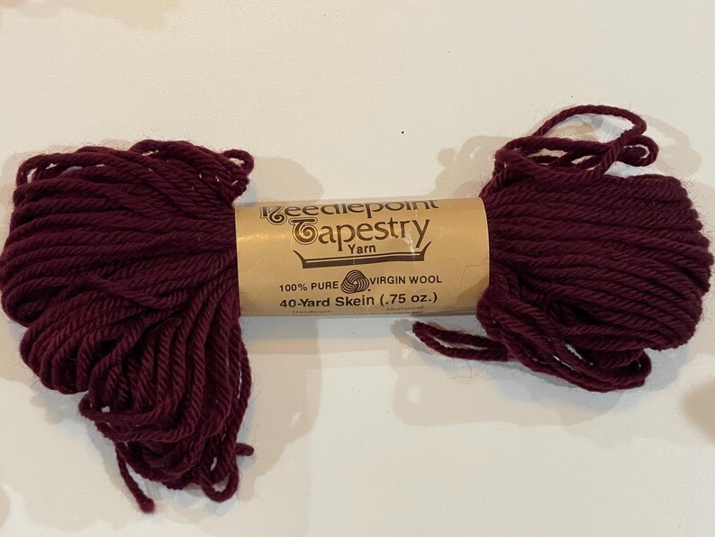 May include: A skein of burgundy wool yarn labeled "Needlepoint Tapestry Yarn" with the details "100% Pure Virgin Wool, 40-Yard Skein (.75 oz.)"
