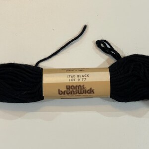 May include: A black skein of yarn with a brown label that reads "1760 BLACK LOT 9 77 Yarns Brunswick".