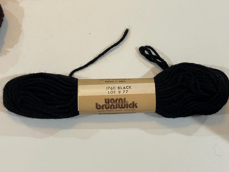 May include: A black skein of yarn with a brown label that reads "1760 BLACK LOT 9 77 Yarns Brunswick".