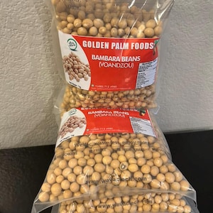 May include: Three bags of dried Bambara beans, also known as Voandzou, from Golden Palm Foods. The bags are stacked on top of each other and are filled with the beige beans. The bags have a label with the company name, product name, and contact information. The label also includes the text "WeVac, waste less, enjoy more."