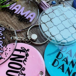 May include: A collection of colorful acrylic keychains with various designs and text. The keychains feature phrases like "My Mama Needs Coffee", "You Got This", and "Dance Dance Dance".
