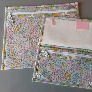 May include: Two floral patterned zippered pouches. The top pouch has a single zipper and the bottom pouch has two zippers. The bottom pouch has a pink felt insert.